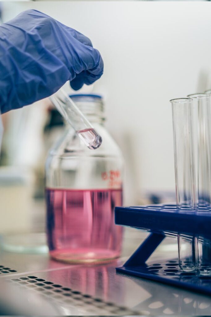 Close-up of a gloved hand handling a test tube with pink liquid in a laboratory setting.